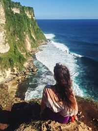 Rear view of woman sitting on cliff against sea