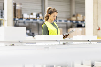 Young worker holding tablet pc analyzing box on conveyor belt in warehouse
