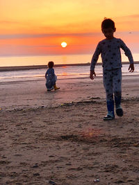 Full length of boys on beach against sky during sunset