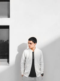 Young man looking away while standing against wall