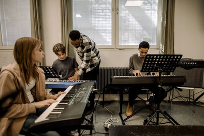 Teacher assisting teenage students during piano class at high school