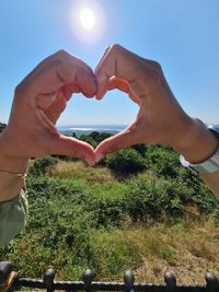 Cropped image of hands making heart shape against sky