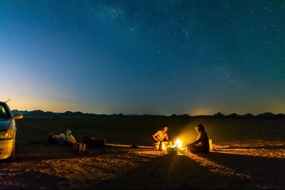 Friends sitting by campfire on field at night