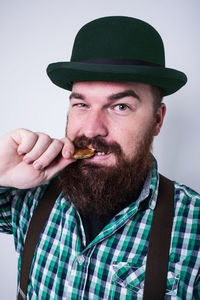 Portrait of hipster biting gold coin while standing against gray background