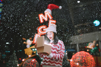 Rear view of woman with arms raised standing against illuminated christmas tree