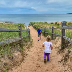 Rear view of sisters walking on sand at beach against sky