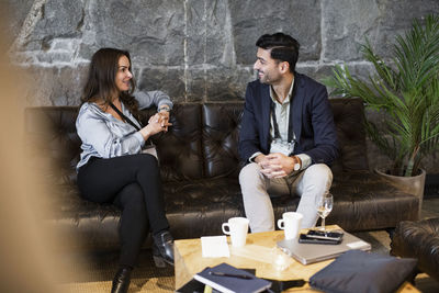 Businesswoman and businessman discussing while sitting on sofa at seminar