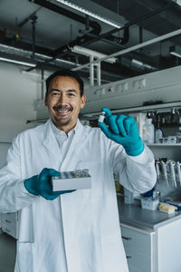 Smiling scientist holding vaccine while standing at laboratory