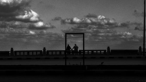 Silhouette people playing soccer on beach against sky