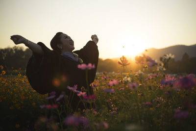 Smiling woman standing on field against sky during sunset