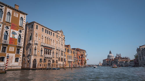 Buildings by river against clear blue sky