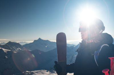Young woman with skis near the hill against the backdrop of the sun's rays. skier, skiing, winter