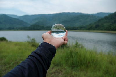 Cropped hand of person holding crystal ball by lake