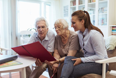 Young woman with grandparents looking at photo album in nursing home