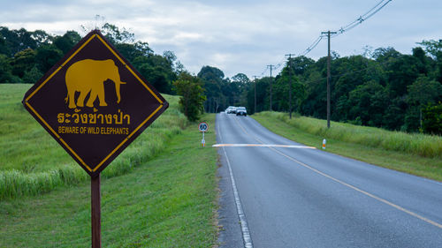 Road sign by trees against sky