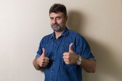 Portrait of mature man gesturing thumbs up while standing against wall