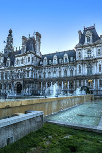 Fountain in front of building against blue sky