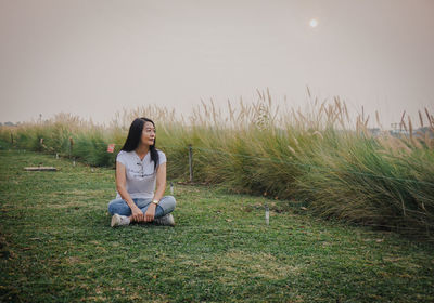 Side view of woman sitting on grassy field