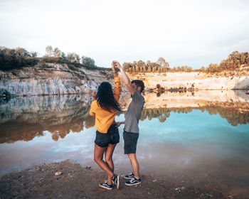 Full length of friends standing by lake against sky