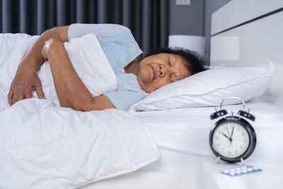 Woman sleeping with alarm clock and medicine on bed