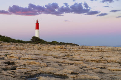 Lighthouse on rock by building against sky