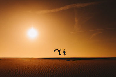 Silhouette people jumping on sand in desert against sky during sunset