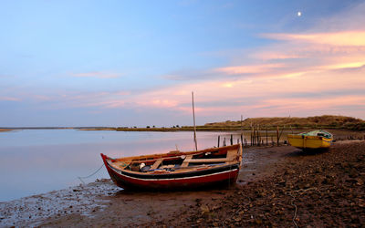 Boat moored on beach against sky during sunset