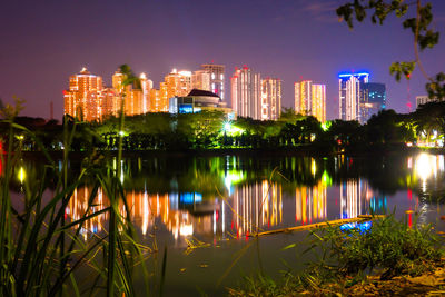 Illuminated buildings by lake against sky in city at night