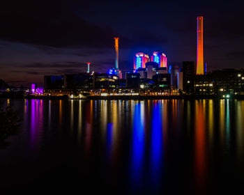 Illuminated city by river against sky at night