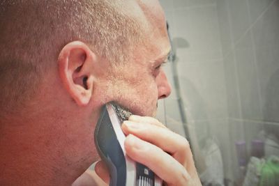 Close-up of man shaving beard with electric razor