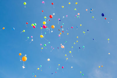 Low angle view of colorful helium balloons flying against blue sky during sunny day