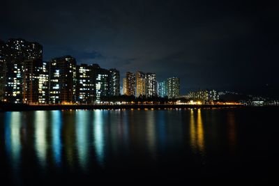 Illuminated city by sea against sky at night