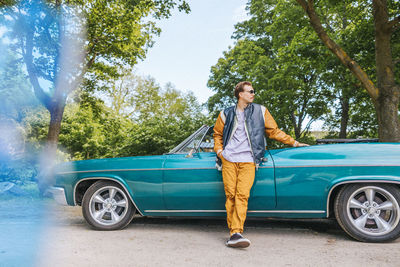 Fashionable man with hand in pocket standing near vintage car at park