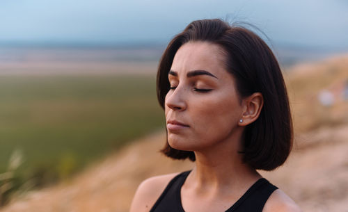 Close-up of young woman looking away at beach against sky