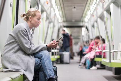 Side view of woman using smart phone sitting in subway train