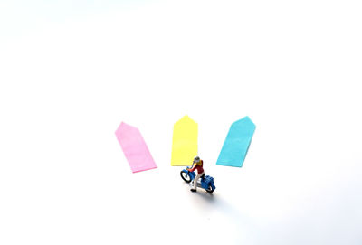 High angle view of biker figurine by arrow shaped adhesive notes over white background