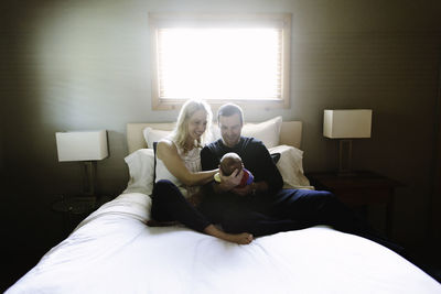 Two new parents smile at their newborn son while sitting on a bed