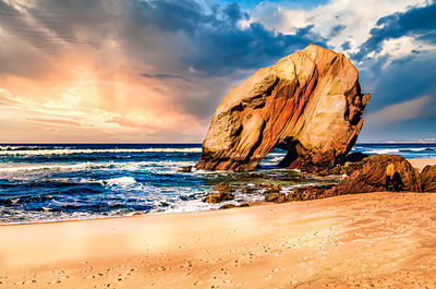 Rock formation on beach against sky during sunset