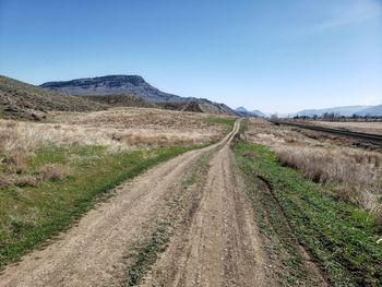 Dirt road leading towards mountains against sky