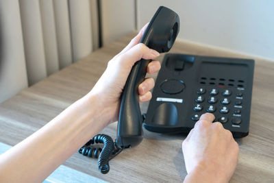 Cropped hands holding telephone on table