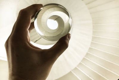 Cropped hand of woman holding crystal ball over spiral staircase