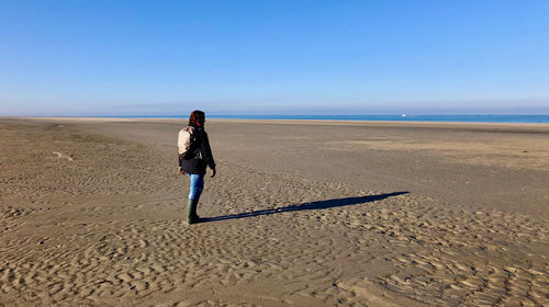 Full length rear view of woman on beach against sky