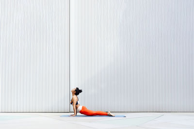 Mid adult female athlete doing cobra pose on mat by wall