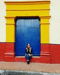 Full length of woman sitting against colorful building in town