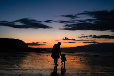 Silhouette of mother and daughter on beach against sky during sunset