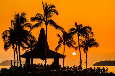 Silhouette palm tree by sea against orange sky