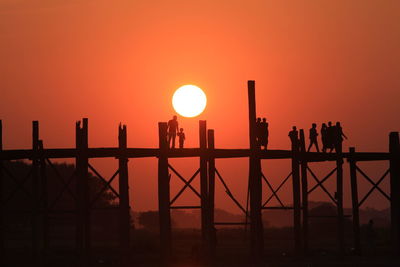 Silhouette people on u bein bridge over river during sunset