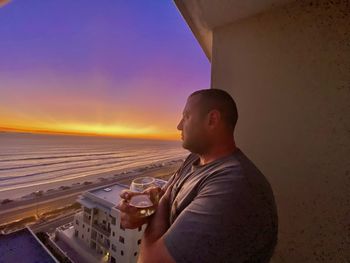 Side view of man looking away while standing against sky during sunset