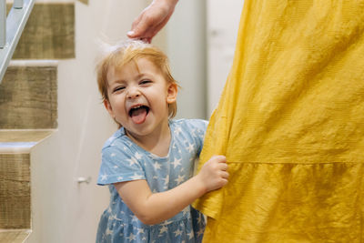 Little playful daughter plays hide and seek behind her mother's skirt.