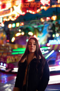 Portrait of smiling young woman standing against illuminated light at night